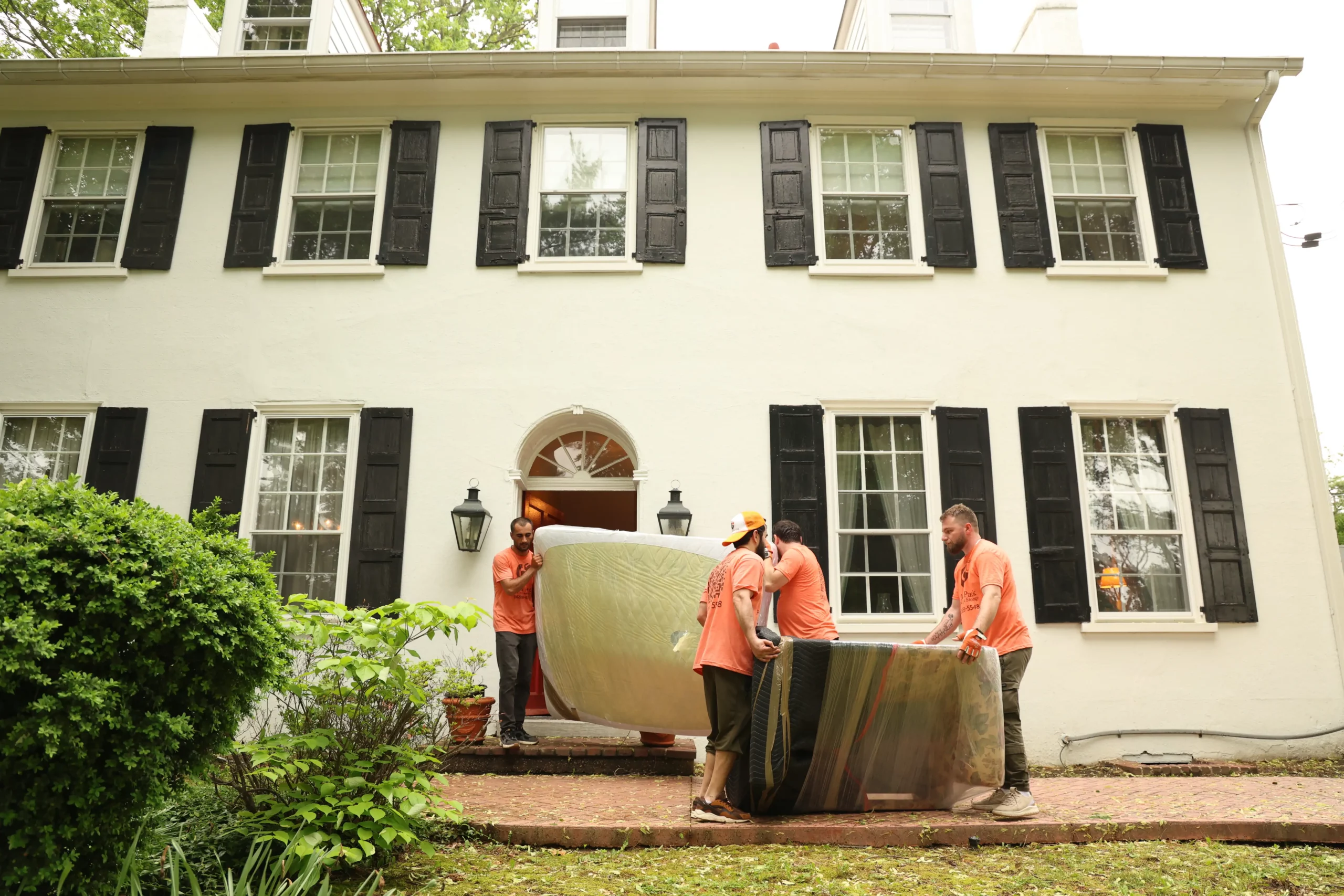 Freehold movers carrying a wrapped mattress out of a home for loading